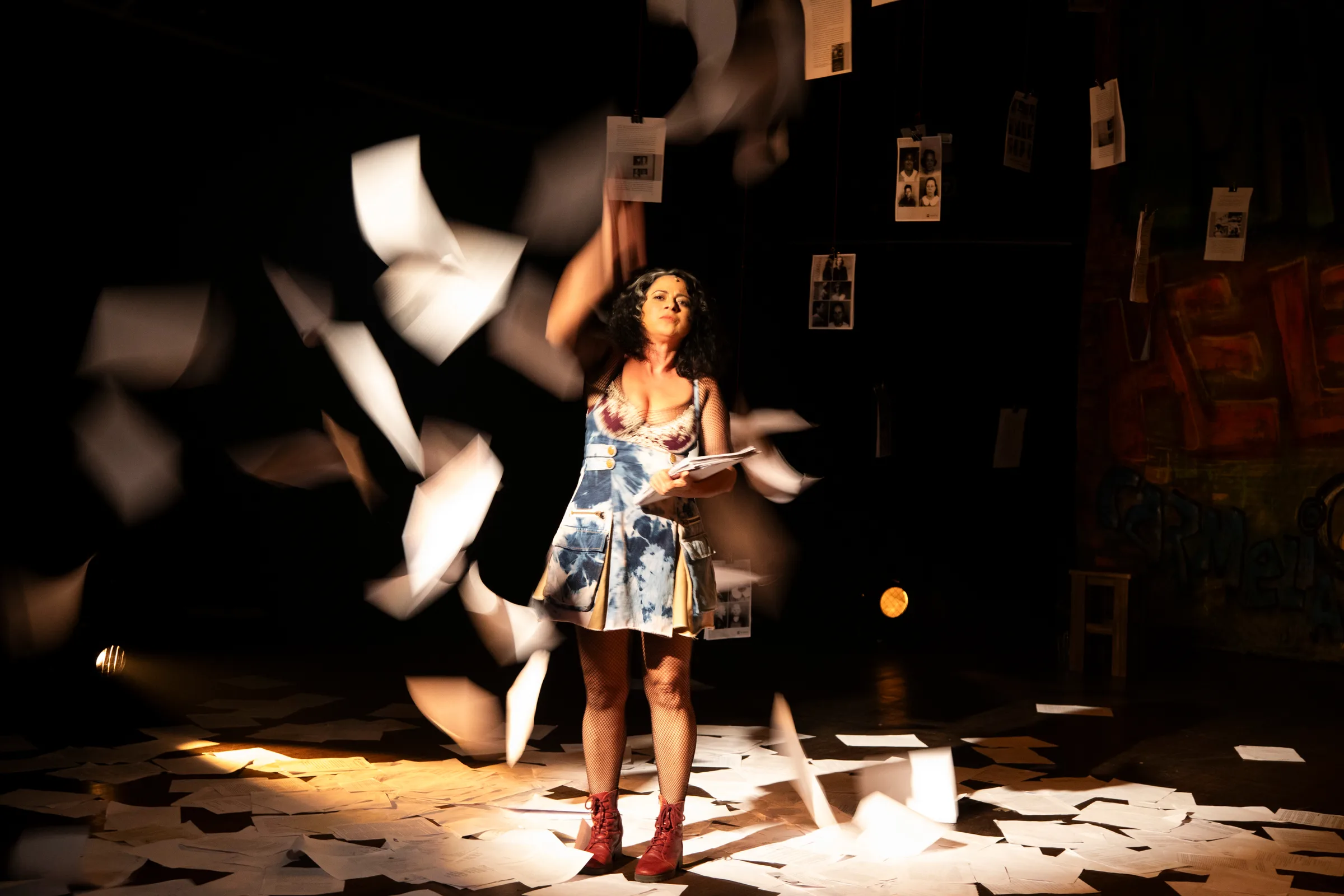 uma mulher em pé no palco ao centro enquanto folhas de papel voam ao redor.